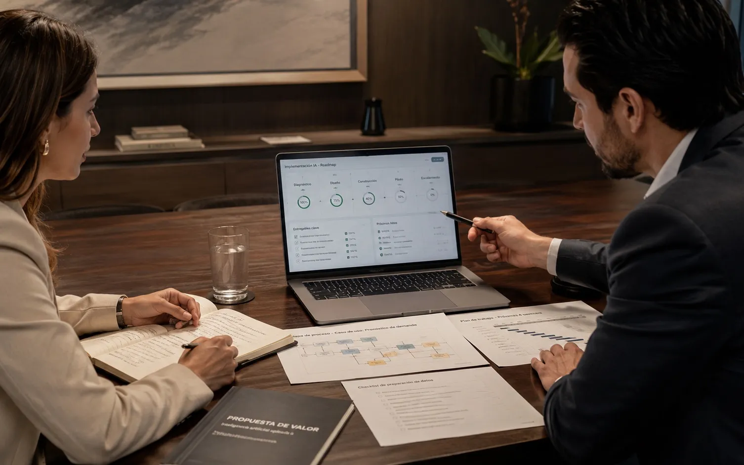 Dos ejecutivos revisando en una laptop el estado de una implementación de IA, junto a un mapa de proceso, un plan de trabajo y un checklist de preparación de datos impresos sobre la mesa.